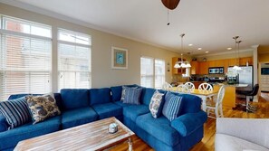 A living room with a blue sectional sofa, a wooden coffee table, and a dining area with a white table and chairs.