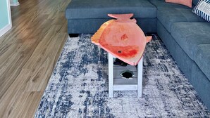 A living room with a sectional sofa, a small table with a fish sculpture, a kitchen in the background, and a dining area. - Salty Shamrock, modern and spacious 2 bedroom, 2 bathroom condo, with ocean views (Carolina Beach)