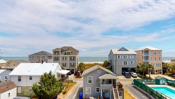 A coastal residential area with houses, a swimming pool, and a beach in the background. - Salty Shamrock, modern and spacious 2 bedroom, 2 bathroom condo, with ocean views (Carolina Beach)