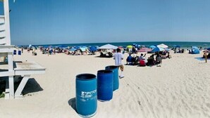 A beach with people, umbrellas, and trash bins. - Salty Shamrock, modern and spacious 2 bedroom, 2 bathroom condo, with ocean views (Carolina Beach)