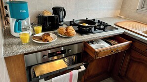 Una cocina con cafetera, tostadora, sartén y un plato de cruasanes.