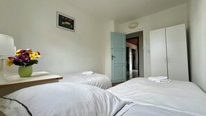 Habitación de hotel con dos camas, una mesita con un florero, un letrero en la pared y un armario.