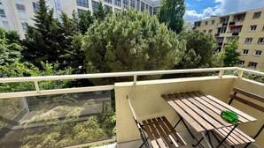 Un balcón con mesa y banco de madera, rodeado de abundante follaje y árboles altos.