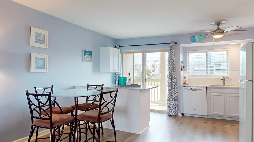 Una cocina moderna con armarios blancos, una zona de comedor con mesa de vidrio y sillas marrones, y un balcón con vistas.