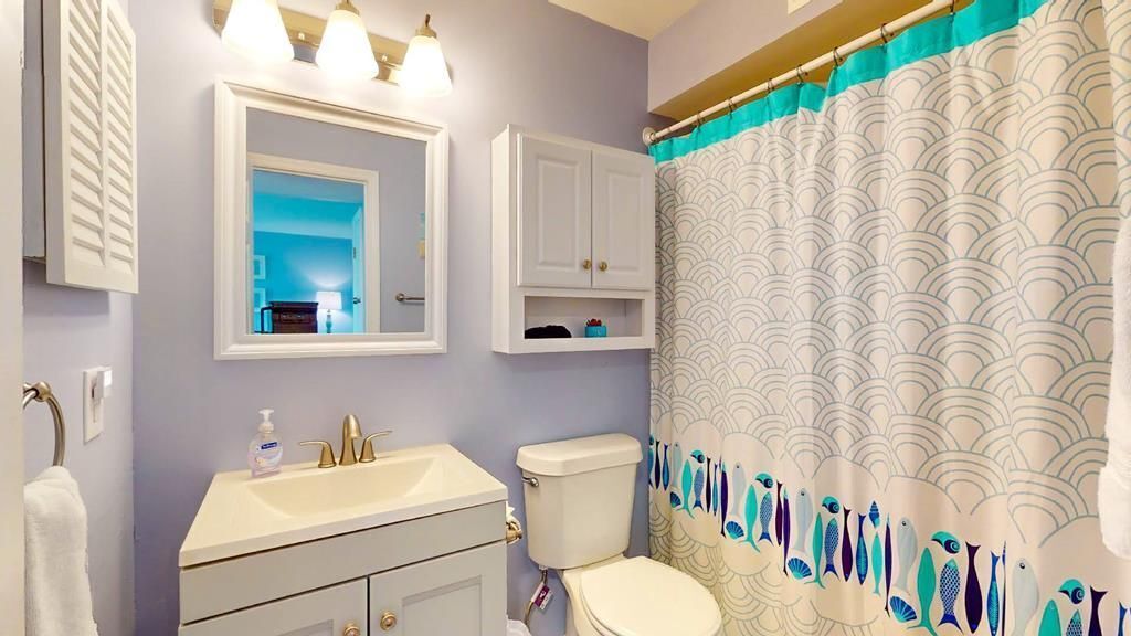 A bathroom with a sink, mirror, toilet, and a shower curtain with a wave pattern.