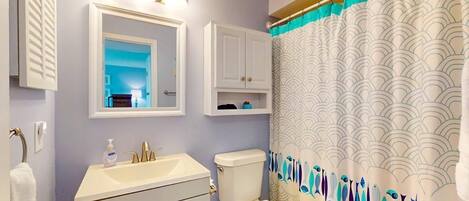 A bathroom with a sink, mirror, toilet, and a shower curtain with a wave pattern.