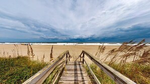 Ein hölzerner Steg führt zu einem Strand unter bewölktem Himmel.
