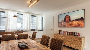 Una sala de reuniones moderna con una mesa de madera, sillas marrones, una estantería y un cuadro grande en la pared.