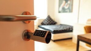 Una puerta moderna con cerradura electrónica, una cama con colcha estampada y un cuadro enmarcado en la pared.