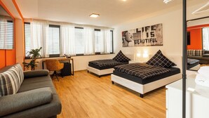 Una habitación de hotel moderna con sofá, dos camas, escritorio y un ventanal con cortinas.