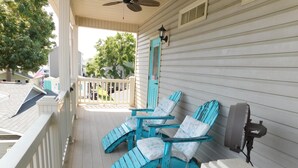 Une véranda avec trois fauteuils Adirondack turquoise, un ventilateur de plafond et un ventilateur fixé au mur.