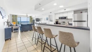 A modern kitchen with bar stools, a dining area with a view, and a living space with a sofa and a TV.