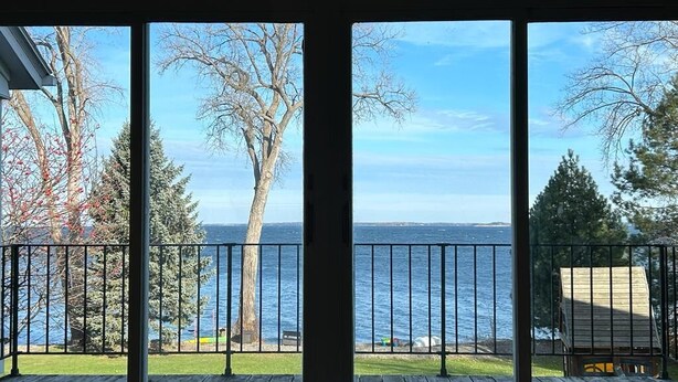 A room with large windows overlooking a body of water, a wooden deck, and a metal railing.