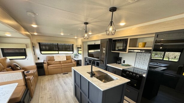 Cocina compacta para vehículos recreativos, con una isla central, zona de comedor con mesa y sillas, y espacio de estar con sofá.