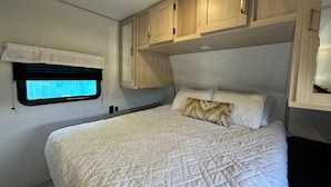 Un dormitorio con cama, ventana y armarios de madera sobre la cama.