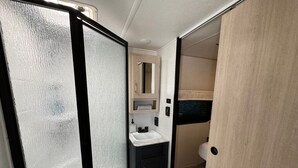 Un baño pequeño con lavamanos blanco, mueble oscuro y un espejo encima.
