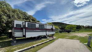 Una vehículo recreativo (RV) estacionado en un camino de grava con césped y árboles al fondo.