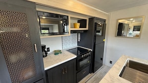 Una cocina compacta con armarios oscuros, microondas integrado, estufa y refrigerador.