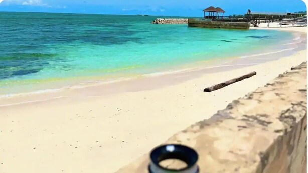 Een strand met helder turquoise water, een zandstrand en een houten pier op de achtergrond.
