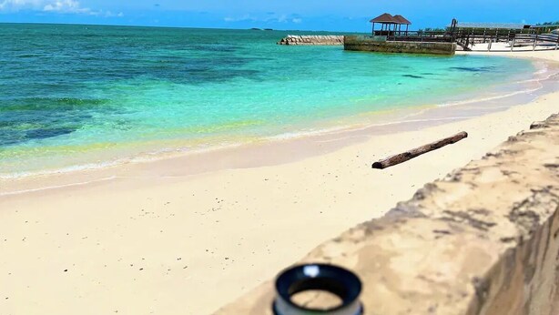 A beach with clear turquoise water, a sandy shore, and a wooden pier with a gazebo. - Oceanfront Cabin (Fresh Creek)