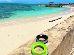 A beach with clear turquoise water, a sandy shore, and a wooden pier with a gazebo.