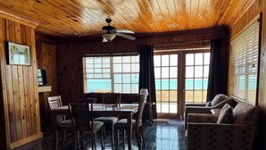 A wooden interior with a dining area, a sofa, and a view of the ocean. - Oceanfront Cabin (Fresh Creek)