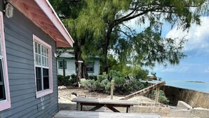 A beachside setting with a wooden picnic table and a white lounge chair. - Oceanfront Cabin (Fresh Creek)