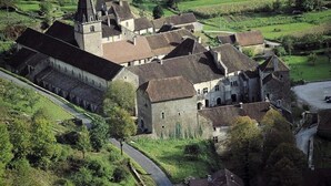 Un grand bâtiment historique, doté de nombreuses ailes et d’une tour imposante, entouré de vastes prairies verdoyantes.
