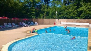 Une piscine où des gens nagent et s’amusent, entourée de chaises longues et de parasols.