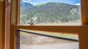 A window view of a mountainous landscape with a dirt road in the foreground.