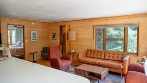 A cozy cabin interior with a wooden interior, a sofa, chairs, and a bed.
