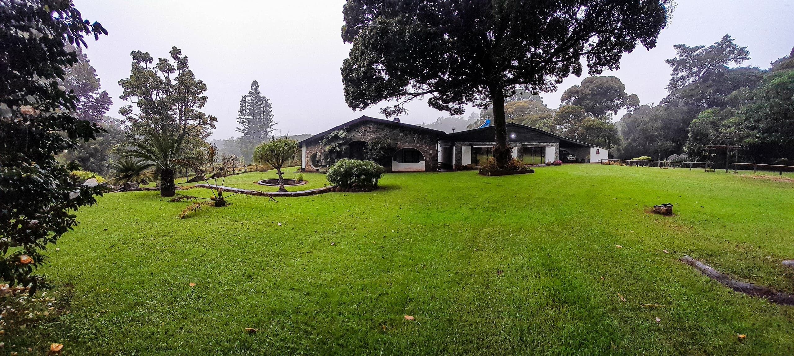 A well-maintained lawn with a stone building, surrounded by trees and a small garden area.