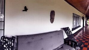 Ein überdachter Außenbereich mit Schachbrettboden, einer Couch und Stühlen.