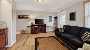 A living room with a fireplace, a black sofa, a TV, and a wooden cabinet. - Cozy Studio Retreat one block from Downtown Noblesville. (Noblesville)