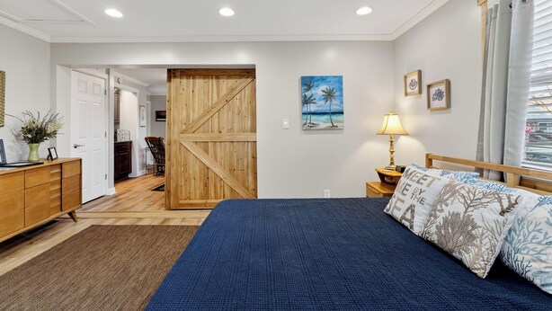 A bedroom with a bed, a wooden door, a painting, and a nightstand with a lamp. - Cozy Studio Retreat one block from Downtown Noblesville. (Noblesville)