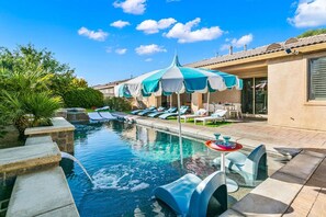 A swimming pool with lounge chairs and umbrellas, a small waterfall feature, and a patio area with outdoor seating. - 3 miles to festivals, fun home, gameroom, deals! (Indio)