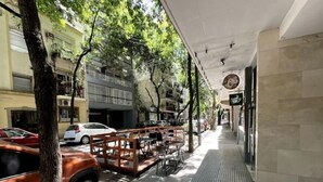 Un marciapiede con tavolini all'aperto, alberi e auto parcheggiate.