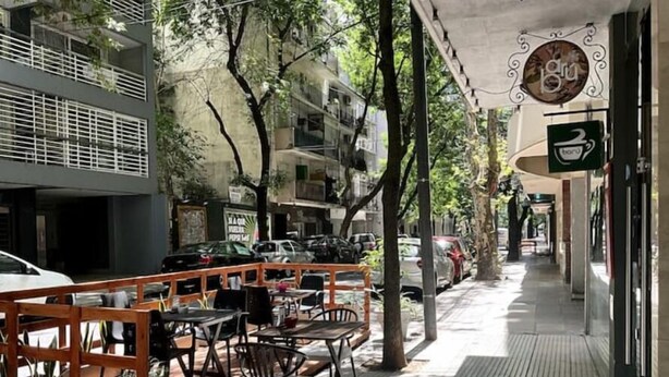 Un caffè all'aperto con tavolini all'esterno, alberi e auto parcheggiate.