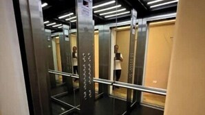 Interno di un ascensore con superfici riflettenti, corrimano metallici e illuminazione a soffitto.