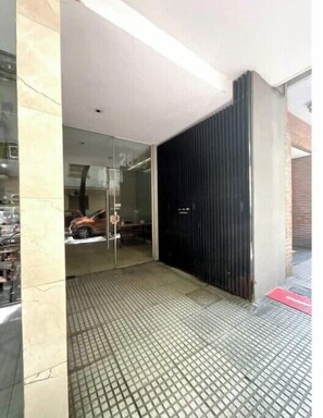 A modern building entrance with a glass door, a metal grid floor, and a black metal wall. - Beautiful studio in Belgrano (Buenos Aires)