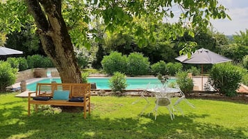 A backyard with a swimming pool, a wooden bench, and a white chair.