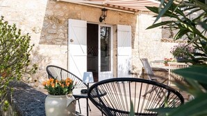 Un edificio de piedra con patio empedrado, una puerta con contraventanas y mobiliario exterior.