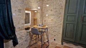 Una habitación pequeña y rústica con pared de piedra, una mesa de madera con una silla, un armario verde y una ventana con vistas.