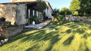 Una casa de piedra con techo de tejas, un jardín delantero con una palmera y un muro de piedra.