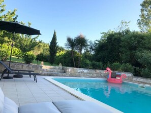 A swimming pool with a pink flamingo float, surrounded by greenery and a stone wall.