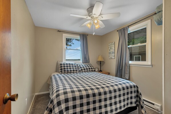 A bedroom with a bed, a ceiling fan, a window with curtains, a nightstand with a lamp, and a wall with a motivational quote. - Beautiful and Clean 2 Bedroom Cottage on Clearwater Lake (South Haven)
