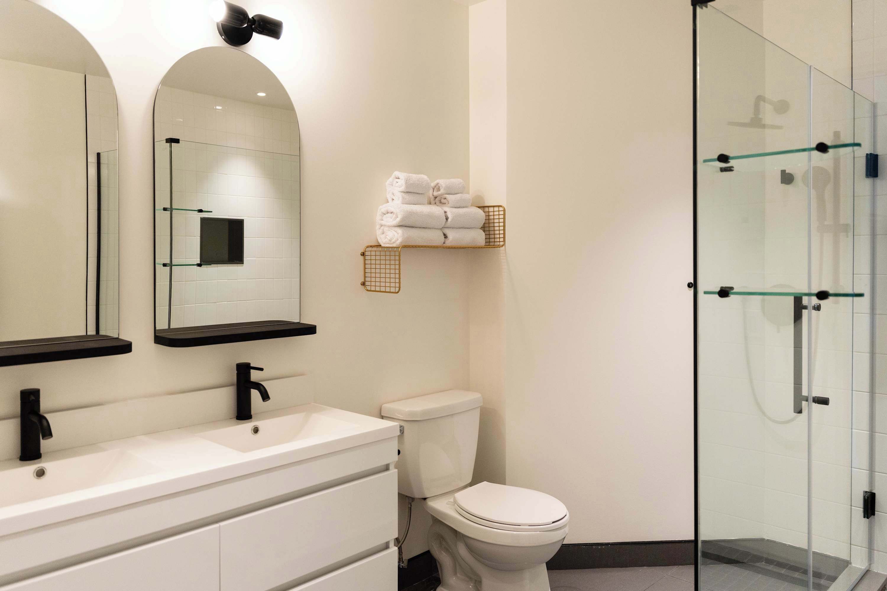 A modern bathroom with a white sink, a toilet, a glass shower enclosure, and a towel rack.