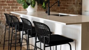 Une cuisine avec un plan de travail blanc, des chaises noires et un robinet noir.