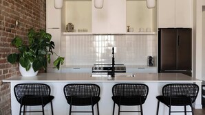 Une cuisine moderne dotée d’un grand îlot central, de quatre tabourets de bar noirs, d’un réfrigérateur en acier inoxydable et d’une plante en pot.