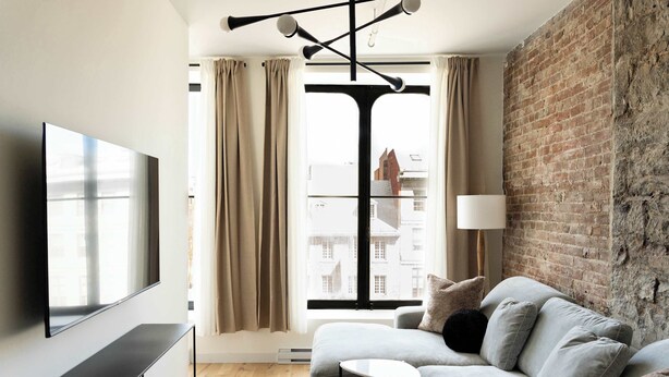 Un salon moderne avec un canapé gris, un téléviseur à écran plat et un mur en briques.